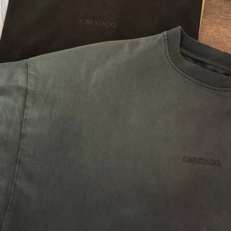 Two Vintage Black tees: a new one on top, one worn for a year below, both with OBRIGADO. tone on tone